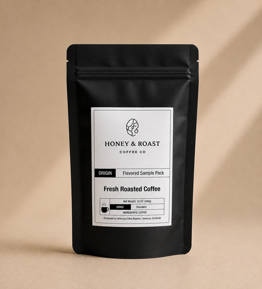 A black stand-up coffee sample pack pouch with a white front label reading Honey & Roast Coffee Co. Fresh Roasted Coffee, photographed on a warm beige background with soft diagonal shadows.
