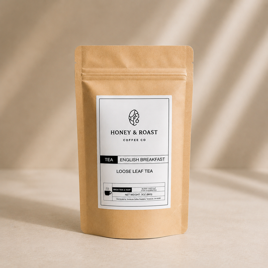 A kraft paper stand-up pouch of Honey & Roast Coffee Co. English Breakfast Loose Leaf Tea, featuring a white label with black text, set against a warm beige background with soft diagonal shadows.