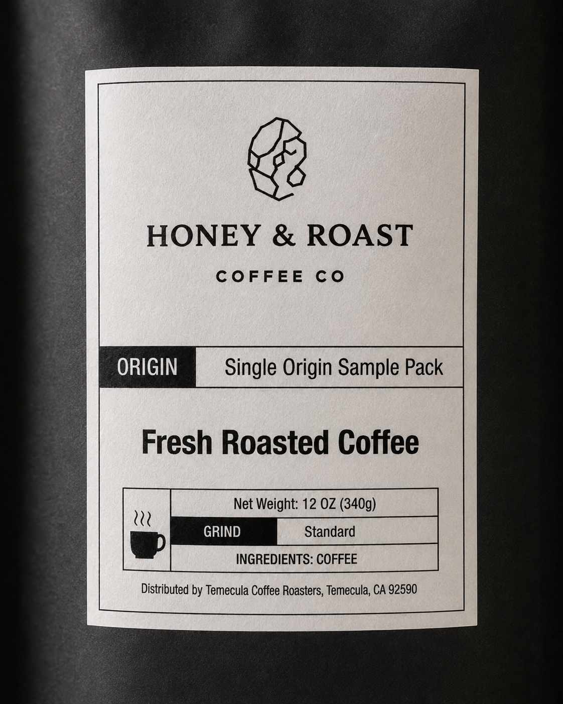 A close-up of a coffee sample pack label from Honey & Roast Coffee Co. The white rectangular label features black text and a simple coffee cup icon, reading 'Origin Single Origin Sample Pack Fresh Roasted Coffee,' with net weight 12 oz (340g), standard grind, and coffee as the ingredient.