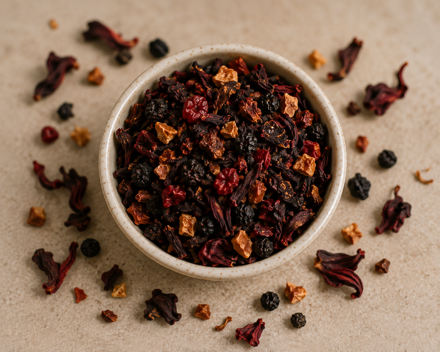 A ceramic bowl filled with loose-leaf herbal tea, surrounded by scattered dried hibiscus flowers and berries on a textured beige surface.