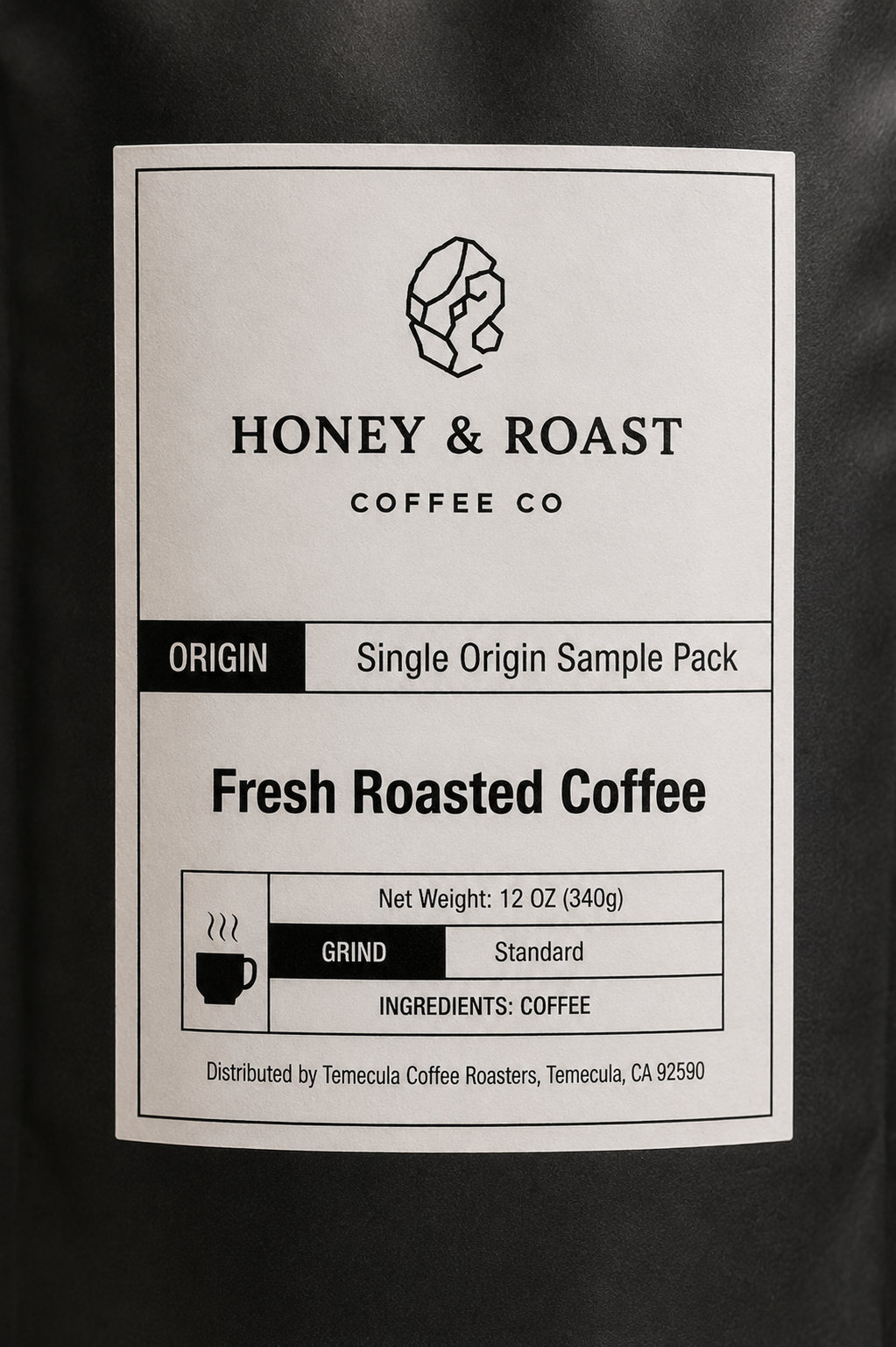 A square white product label for Honey & Roast Coffee Co. Single Origin Sample Pack, featuring black text and a simple coffee cup icon, photographed against a dark background.