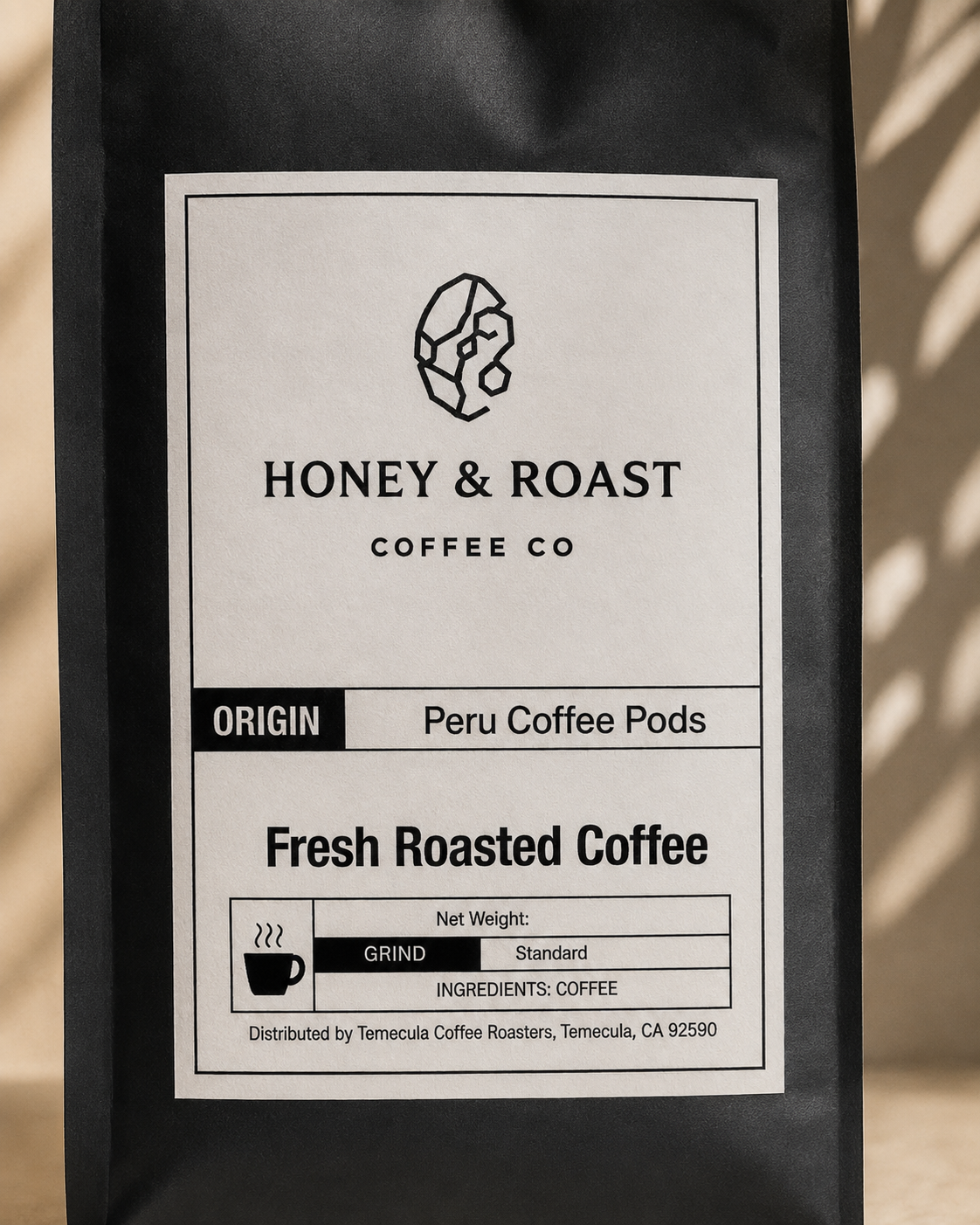 A black coffee bag with a large white label reading Honey & Roast Coffee Co, Peru Coffee Pods, and Fresh Roasted Coffee, photographed outdoors with soft shadow patterns on the right side.