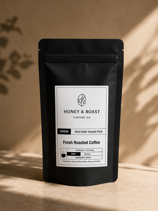 A black stand-up coffee bag with a white front label reading Honey & Roast Coffee Co. Fresh Roasted Coffee, placed on a beige surface with warm sunlight and leaf shadows.