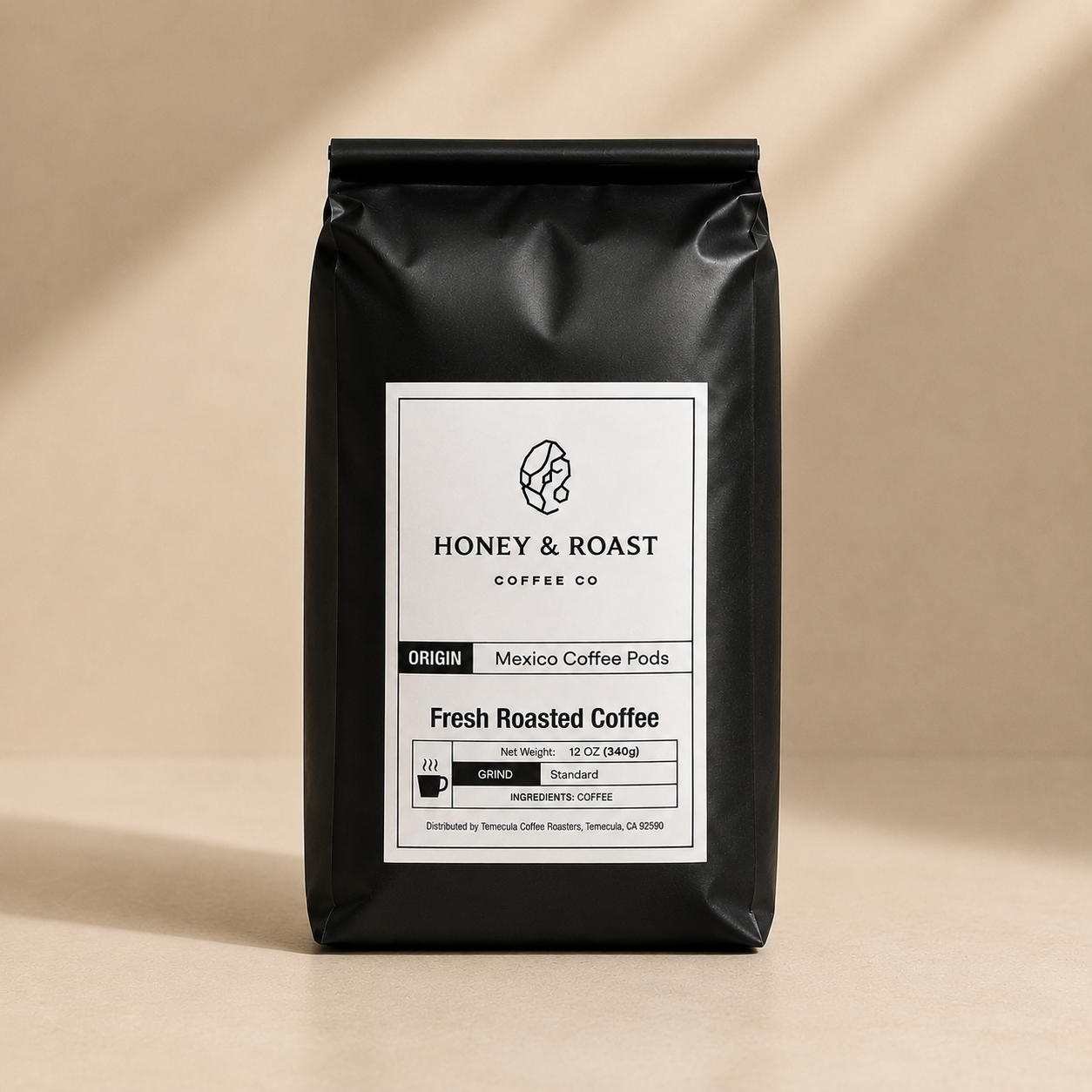 A black bag of Honey & Roast Coffee Co. Fresh Roasted Coffee, Mexico Coffee Pods, standing upright on a beige surface with soft diagonal shadows.