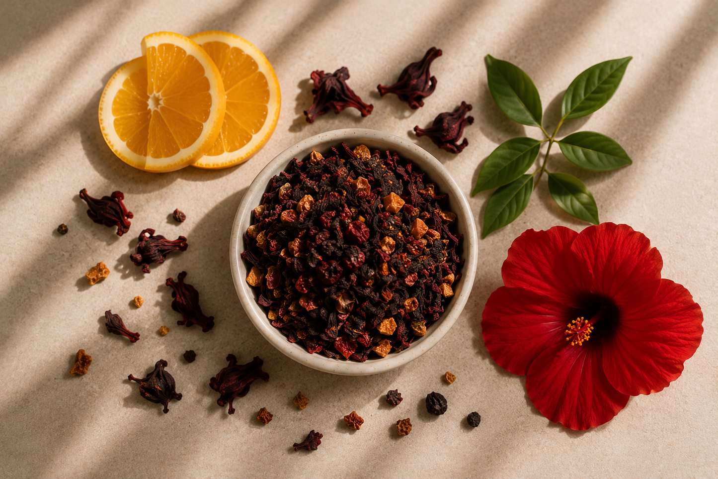 A styled flat-lay of a white bowl filled with dark dried hibiscus tea, surrounded by ingredients including two orange slices, a large red hibiscus flower, scattered dried flowers, and green leaves on a beige textured surface with soft shadows.